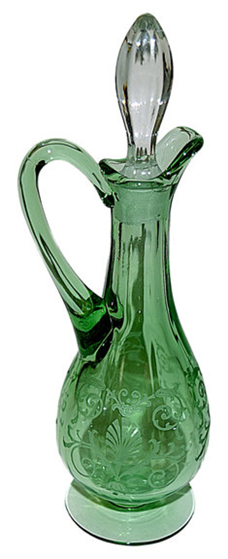 May include: A green glass bottle with a clear glass stopper and a decorative etched design. The bottle has a handle and a round base.