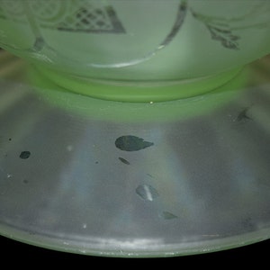 May include: A pale green glass vase with a frosted finish and a wide base. The vase has a delicate floral design etched into the glass.