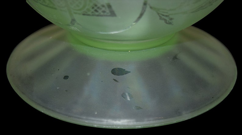 May include: A pale green glass vase with a frosted finish and a wide base. The vase has a delicate floral design etched into the glass.