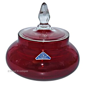 May include: A red glass candy jar with a clear glass lid and a clear glass knob. The jar has a label that reads "Old Genuine Lead Crystal Made in USA Morgantown".
