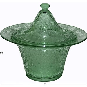 May include: A green glass serving dish with a lid. The dish is 6 1/4 inches tall and 7 inches wide. It features a floral pattern etched into the glass. The lid has a small knob on top.