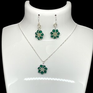 May include: A silver necklace and earrings set with a green crystal flower pendant and matching earrings.