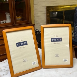 May include: Two rectangular picture frames with light brown wooden borders. Each frame contains a white insert with the text Burnes State Street and For Your 8x12 Photograph. A small white barcode sticker is attached to the bottom corner of each.
