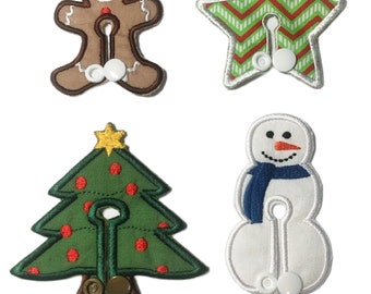 May include: Four Christmas-themed fabric patches with a button and loop closure. The patches are shaped like a gingerbread man, a star, a Christmas tree, and a snowman.