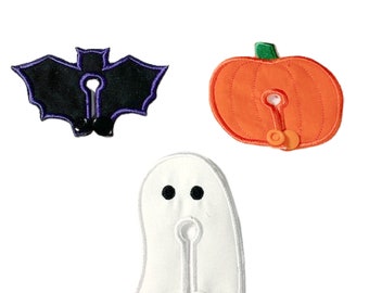 May include: Three Halloween-themed fabric patches with a buttonhole and button. The patches are a black bat, an orange pumpkin, and a white ghost.