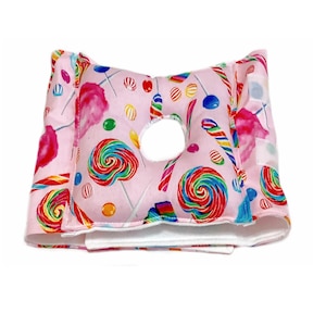 May include: A pink pillow with a hole in the center, covered in a candy-themed fabric featuring lollipops, candy canes, and cotton candy.