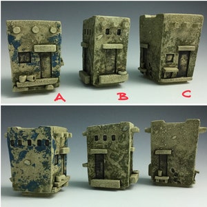 May include: Three ceramic planters in the shape of small houses. The planters are decorated with a rustic, textured finish. One planter is painted blue and white, while the other two are green and brown. Each planter has a small window and a door.