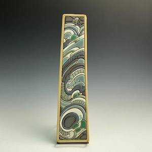May include: A tall, rectangular ceramic vase with a cream-colored frame. The vase features a detailed, abstract design in shades of blue, gray, and green. The design includes swirling patterns and organic shapes, creating a unique decorative piece.