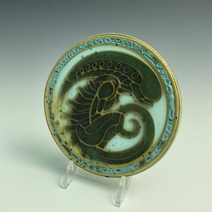 May include: A round, ceramic coaster with a green and blue alien design. The alien is stylized and has a white background.