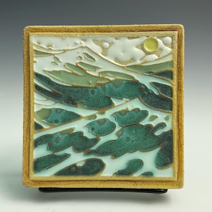 May include: Square ceramic tile with a landscape design. The artwork features a stylized ocean scene with green and teal waves, white clouds, and a yellow sun against a light blue background. The tile is framed with a textured, golden-brown border.