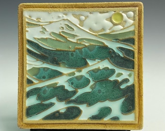 Könnte beinhalten: Quadratische Keramikfliese mit Landschaftsmotiv. Das Kunstwerk zeigt eine stilisierte Meereslandschaft mit grünen und türkisfarbenen Wellen, weißen Wolken und einer gelben Sonne vor hellblauem Hintergrund. Die Fliese hat einen strukturierten, goldbraunen Rand.