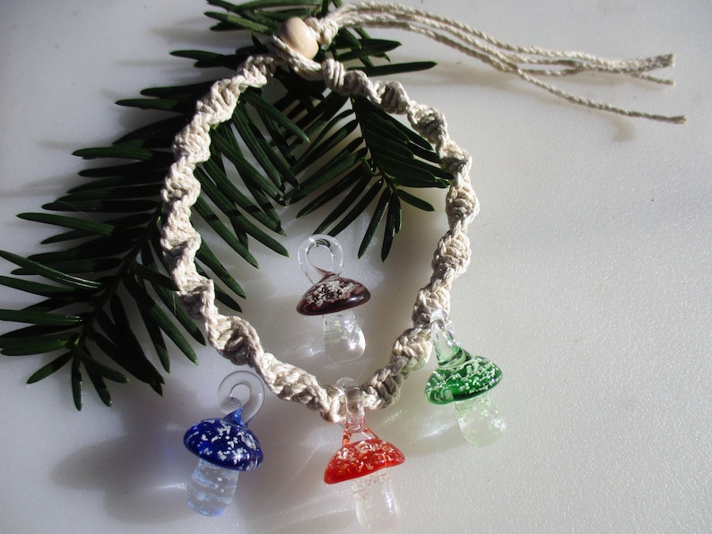 May include: A macrame necklace with four glass mushroom charms. The charms are in shades of red, green, blue, and brown.