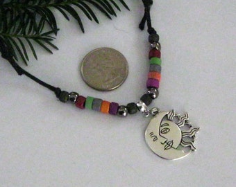 May include: A black cord necklace with a silver sun pendant and colorful beads. The beads are purple, orange, green, and gray.