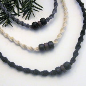 May include: Three necklaces with wooden beads. The necklaces are made of black, white, and gray cord. The beads are brown and black.