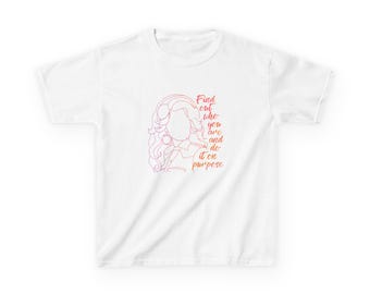 Op de afbeelding: Een wit T-shirt met korte mouwen en een rood-oranje verloop-lijnillustratie van een persoon met volumineus haar. De tekst "Find out who you are and do it on purpose" is in een cursief lettertype naast de illustratie gedrukt.