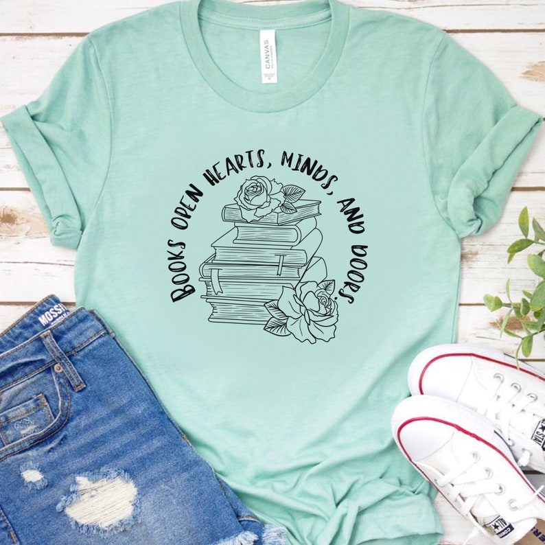May include: A light green t-shirt with a black graphic design that says "Books open hearts, minds and doors." The graphic also features a stack of books with a rose on top.