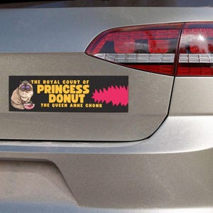 Könnte beinhalten: Ein rechteckiger Autoaufkleber mit schwarzem Hintergrund, der eine flauschige Katze mit violetter Sonnenbrille und Krone neben einem rosa Donut zeigt. Der Text lautet: THE ROYAL COURT OF PRINCESS DONUT THE QUEEN ANNE CHONK in Gelb und Weiß.