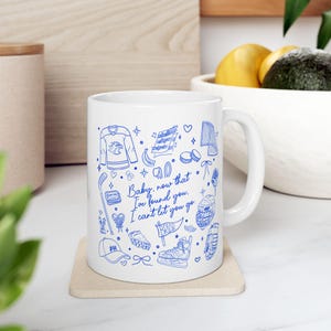 Puede incluir: Una taza de cerámica blanca con ilustraciones de línea azul de equipo de hockey, notas musicales, un corazón y el texto: Baby, now that I've found you. I can't let you go. El diseño incluye una camiseta de hockey, un palo, patines, casco y un banderín.