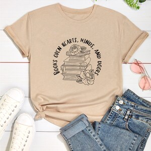 May include: A beige t-shirt with a graphic of a stack of books and roses with the text "Books open hearts, minds, and doors".