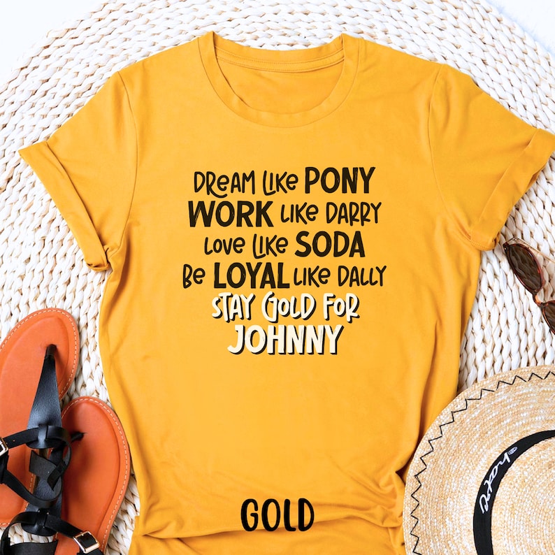 K&ouml;nnte beinhalten: Gelbes T-Shirt mit schwarzem Text, der "Dream like Pony, Work like Darry, Love like Soda, Be Loyal like Dally, Stay Gold for Johnny" lautet. Das Wort "Gold" ist in Schwarz am unteren Rand des Shirts gedruckt.