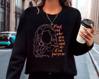 Könnte beinhalten: Schwarzer Pullover mit einer rosa und orangefarbenen Linienzeichnung einer Frau mit langen Haaren und dem Text "Find out who you are and do it on purpose".