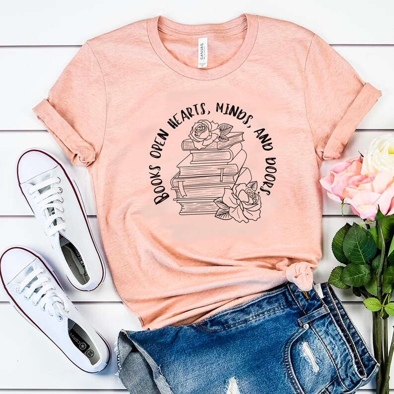 May include: A peach-colored t-shirt with a black graphic of a stack of books with roses and the text "Books open hearts, minds, and doors."