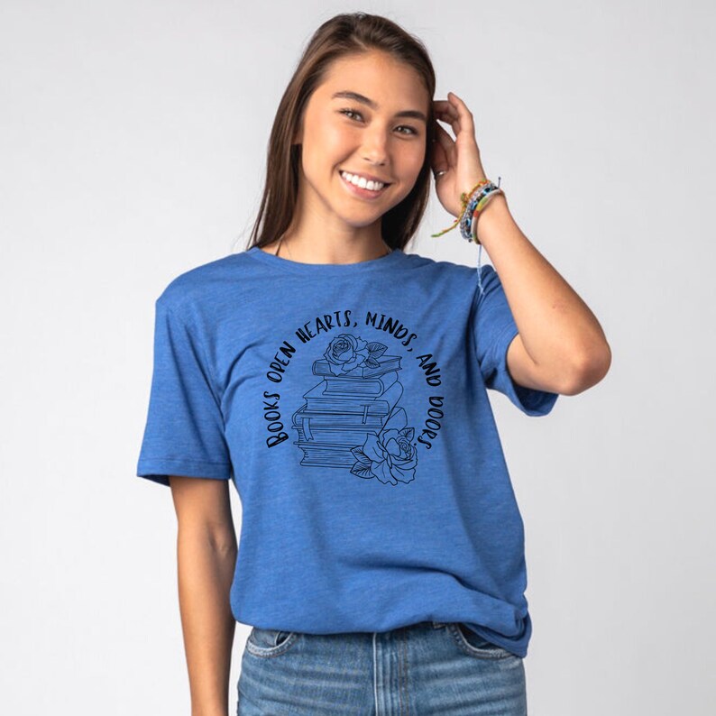 May include: A blue t-shirt with a black graphic design featuring a stack of books with a rose on top. The text around the books reads "Books open hearts, minds, and doors".