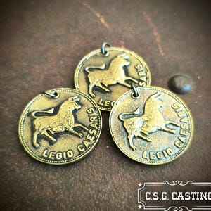 May include: Three circular brass-toned metal pendants featuring a raised relief of a bull in the center. Each pendant is inscribed with the text LEGIO CAESARIS along the bottom edge and includes a small metal loop at the top for attachment.