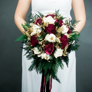 Small winter wedding bridesmaid bridal bouquet with burgundy and ivory sola roses, pine cones, gold dried flowers and preserved greenery