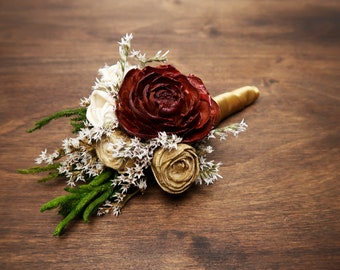 May include: A burgundy, gold, and white wooden flower bouquet with greenery. The bouquet is tied with a gold ribbon.