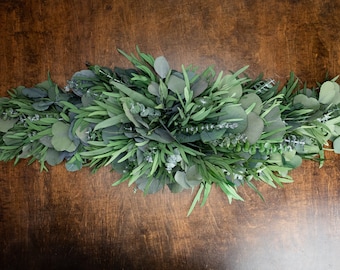May include: A green eucalyptus garland with a mix of different leaf sizes and textures. The garland is perfect for adding a touch of greenery to any space.