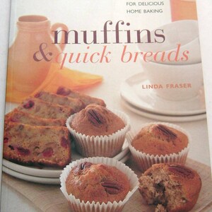 May include: A cookbook titled "Muffins & Quick Breads" by Linda Fraser. The cover features a close-up of muffins with pecans and a loaf of cranberry bread.