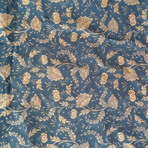 May include: A blue fabric with a repeating pattern of gold floral designs. The pattern features stylized flowers and leaves.
