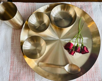 May include: A set of brass bowls and a spoon on a large brass plate. The plate has a shiny, reflective surface. There are four red roses on the plate.