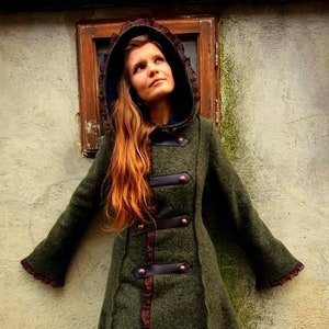 May include: A long, green wool coat with a brown leather trim and a lace trim. The coat has a hood and a button closure. The model is wearing the coat with black tights and brown boots.