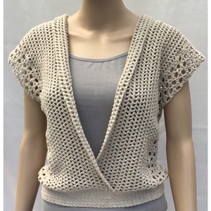 May include: A crocheted cream-colored vest with a deep V-neck and short sleeves. The vest has a delicate openwork pattern and a crocheted band at the bottom.