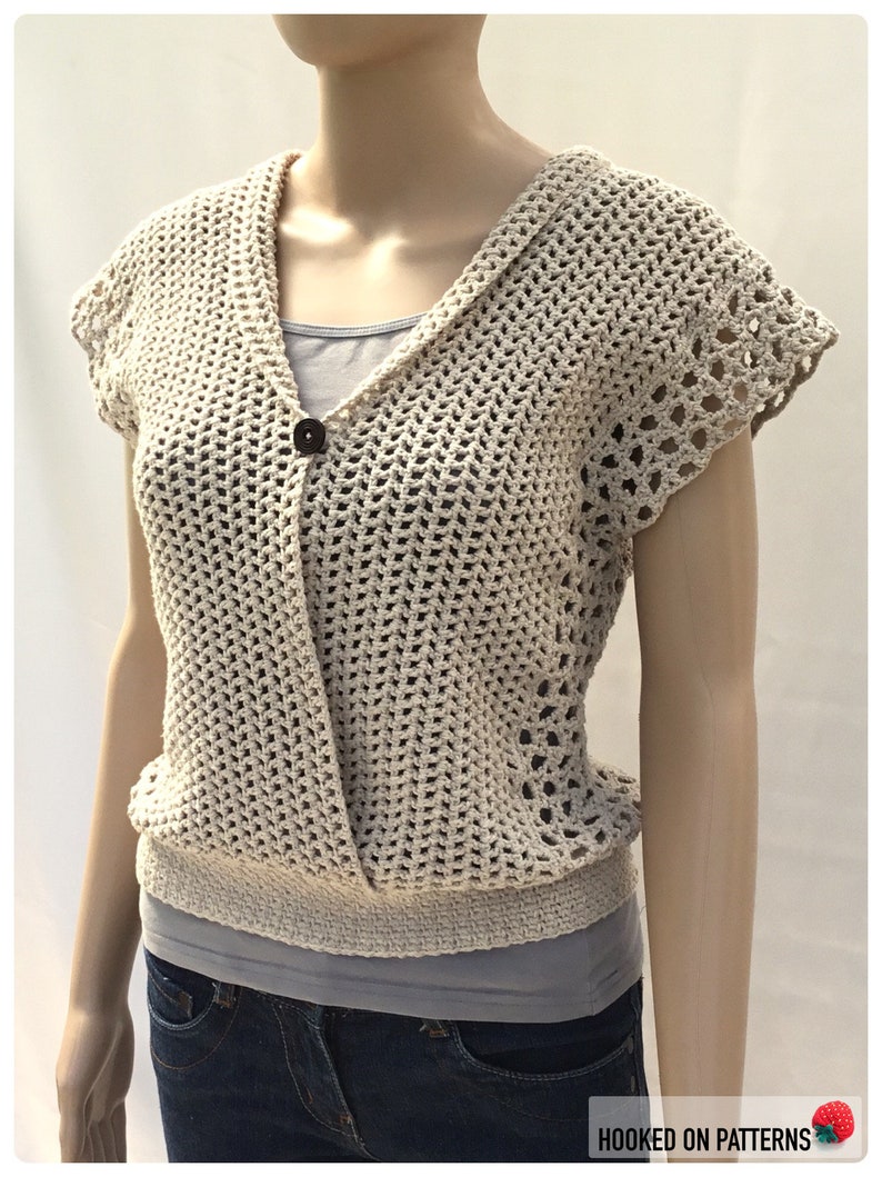 May include: A crocheted cream-colored sleeveless top with a V-neck and a single button closure. The top has a delicate openwork pattern and a slightly fitted silhouette.