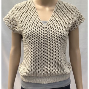 May include: A beige crochet top with a v-neck and short sleeves. The top has a loose, open weave and a crocheted border around the neckline and sleeves.