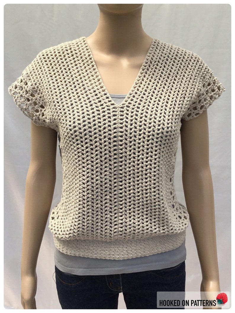 May include: A beige crochet top with a v-neck and short sleeves. The top has a loose, open weave and a crocheted border around the neckline and sleeves.