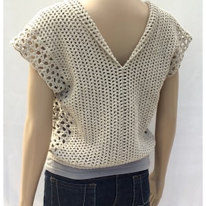 May include: A crocheted top with a V-neck and short sleeves. The top is made in a beige color and has a lacy pattern. The top is being worn by a mannequin.