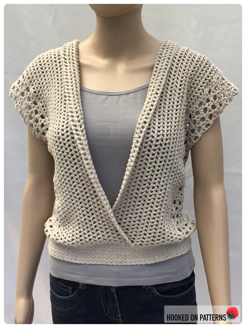 May include: A crocheted cream-colored vest with a deep V-neck and short sleeves. The vest has a delicate openwork pattern and a crocheted band at the bottom.