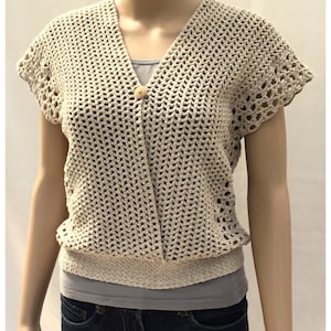 May include: A crocheted beige top with a V-neck and short sleeves. The top has a button closure and a crocheted band at the bottom.