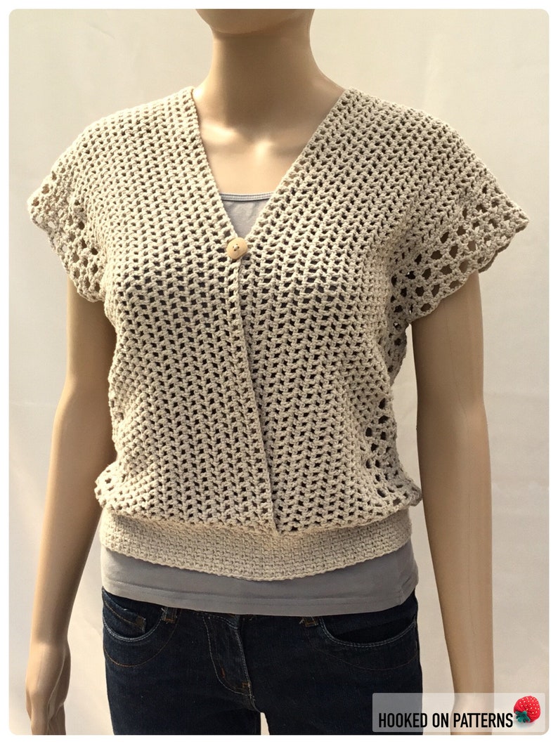 May include: A crocheted beige top with a V-neck and short sleeves. The top has a button closure and a crocheted band at the bottom.