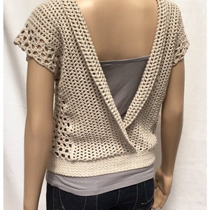 May include: A beige crochet top with a deep V-back and short sleeves. The top is made with a lacy stitch and has a ribbed hem.