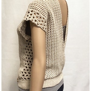 May include: A crocheted top with a low back and short sleeves. The top is made with a beige yarn and has a lacy pattern.