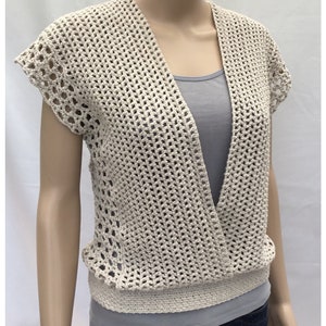 Puede incluir: Un top de color beige tejido a crochet con cuello en V profundo y mangas cortas. El top tiene un patrón de encaje y una banda de crochet en la parte inferior.