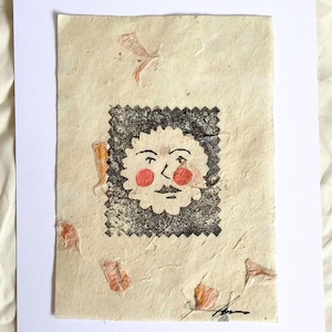 Puede incluir: Una impresión artística hecha a mano que presenta una cara caprichosa con mejillas rosadas y un bigote, enmarcada por un borde negro texturizado. La obra de arte está sobre papel texturizado con acentos coloridos.