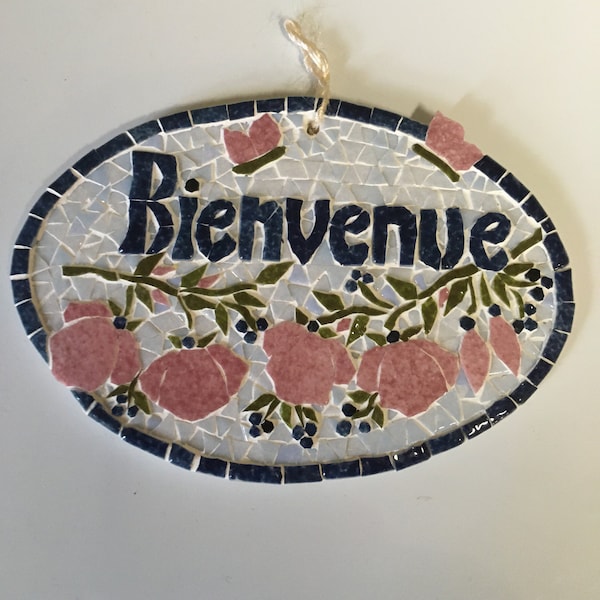 Plaque de porte en mosaïque: "Bienvenue. "Guirlande de fleurs roses et cordelette de fixation sur un support en bois peint.