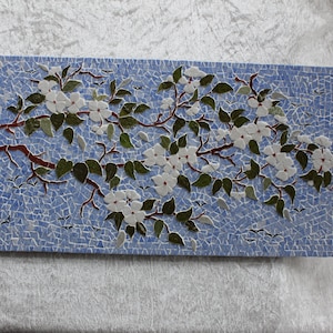 Mosaikmalerei: Apfelbaumzweig, der im Wind auf Hintergrund des blauen Himmels schwankt. Größe 42 cm x 21,5 cm. Ständer aus Holz.