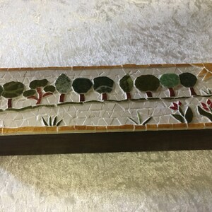 May include: A wooden box with a mosaic tile design featuring a row of green trees with red trunks and a row of red flowers with green leaves.